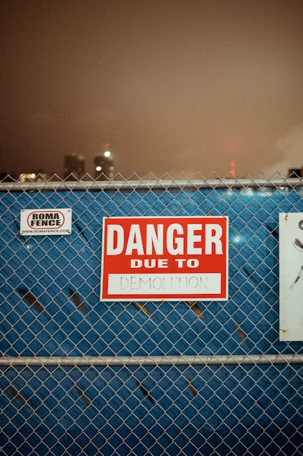 Fenced excavation site at night with gate lights and visible perimeter security