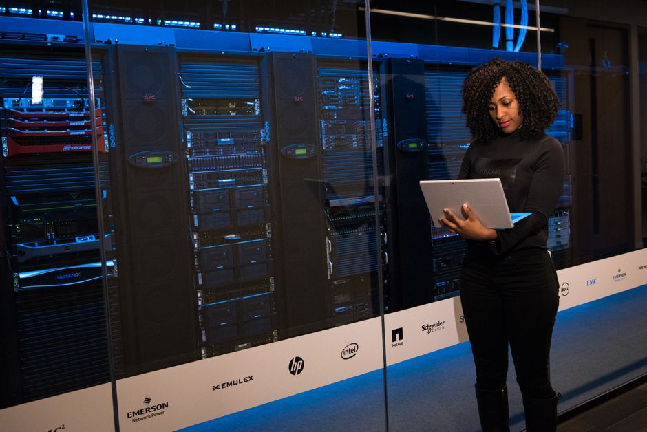 Technician monitoring network security in a server room while reviewing alerts and dashboards